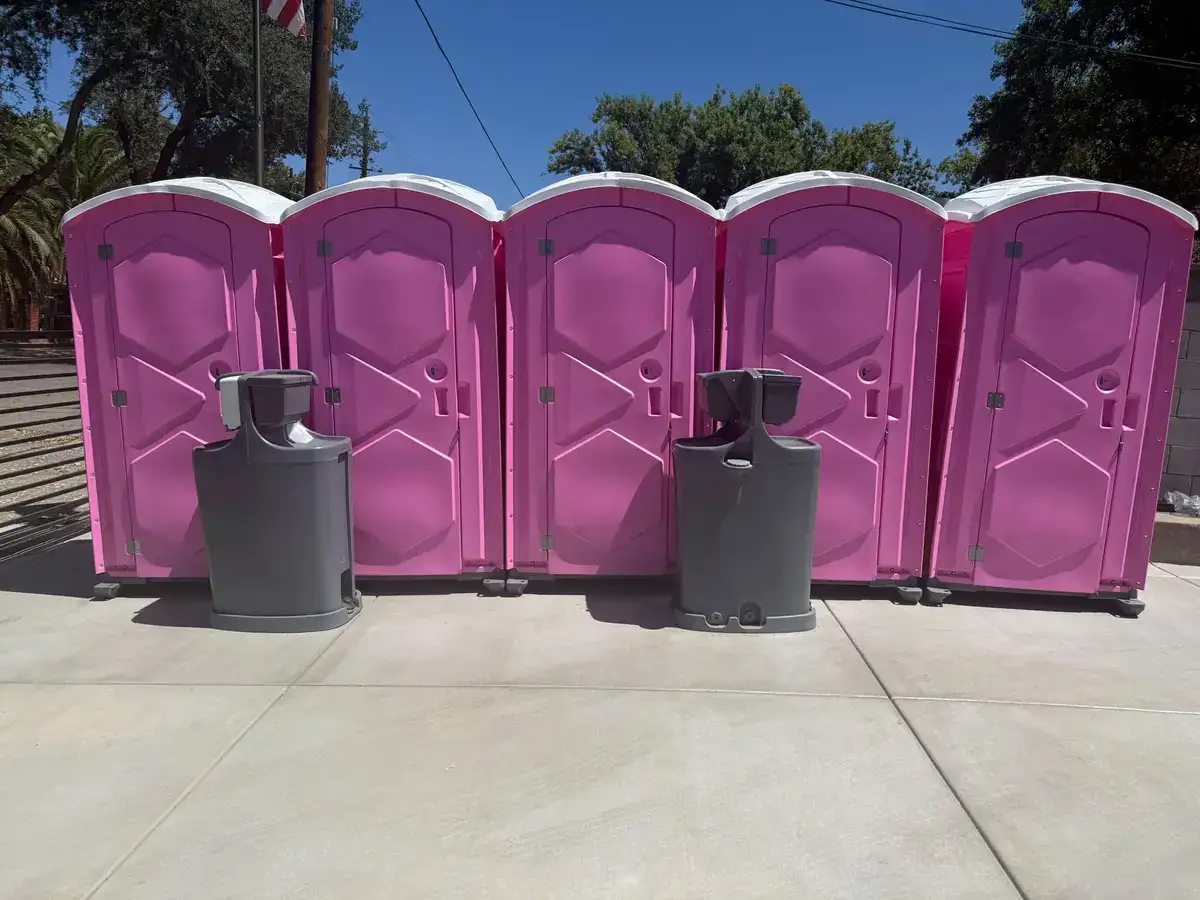 Five pink portable toilets with two hand wash stations set up in a row