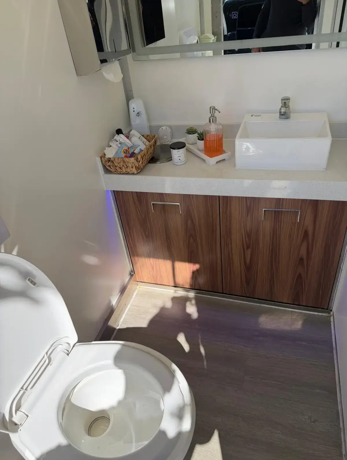 Inside a restroom trailer: vessel sink, wood vanity and lit mirror