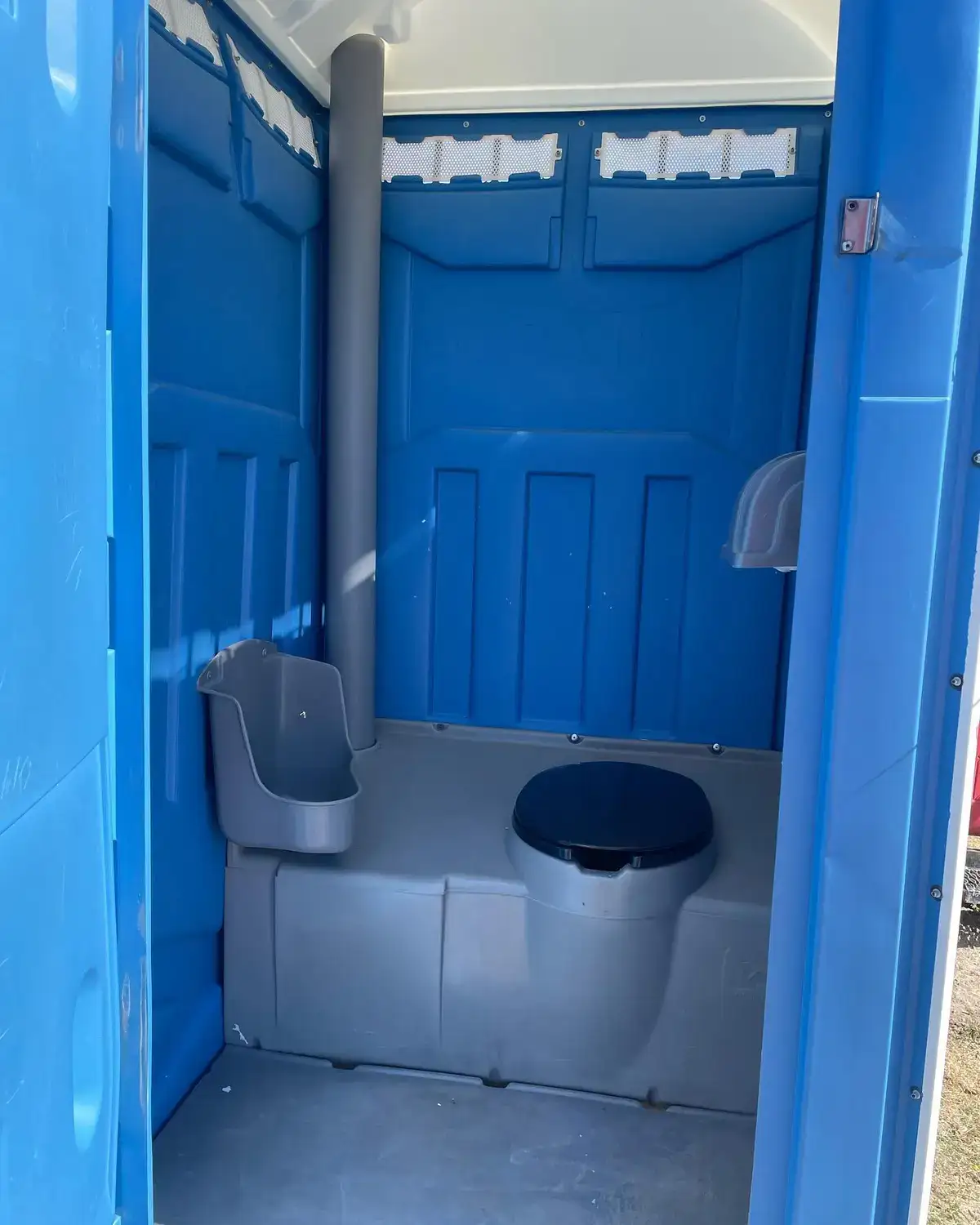 Inside a blue standard portable toilet: urinal, seat and vent pipe