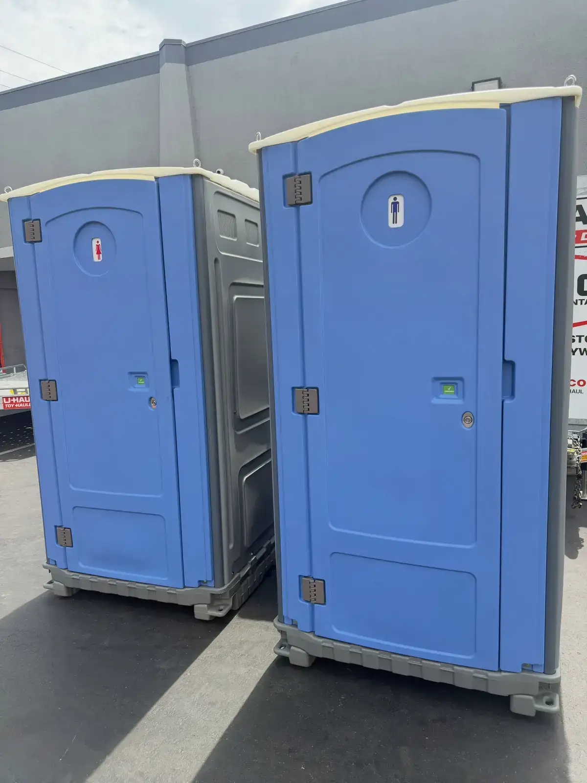 Two blue standard portable toilets side by side on pavement